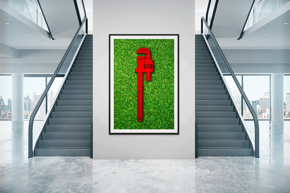 Photograph of a bold red pipe wrench laid flat on vibrant green grass, contrasting industrial form with natural texture.