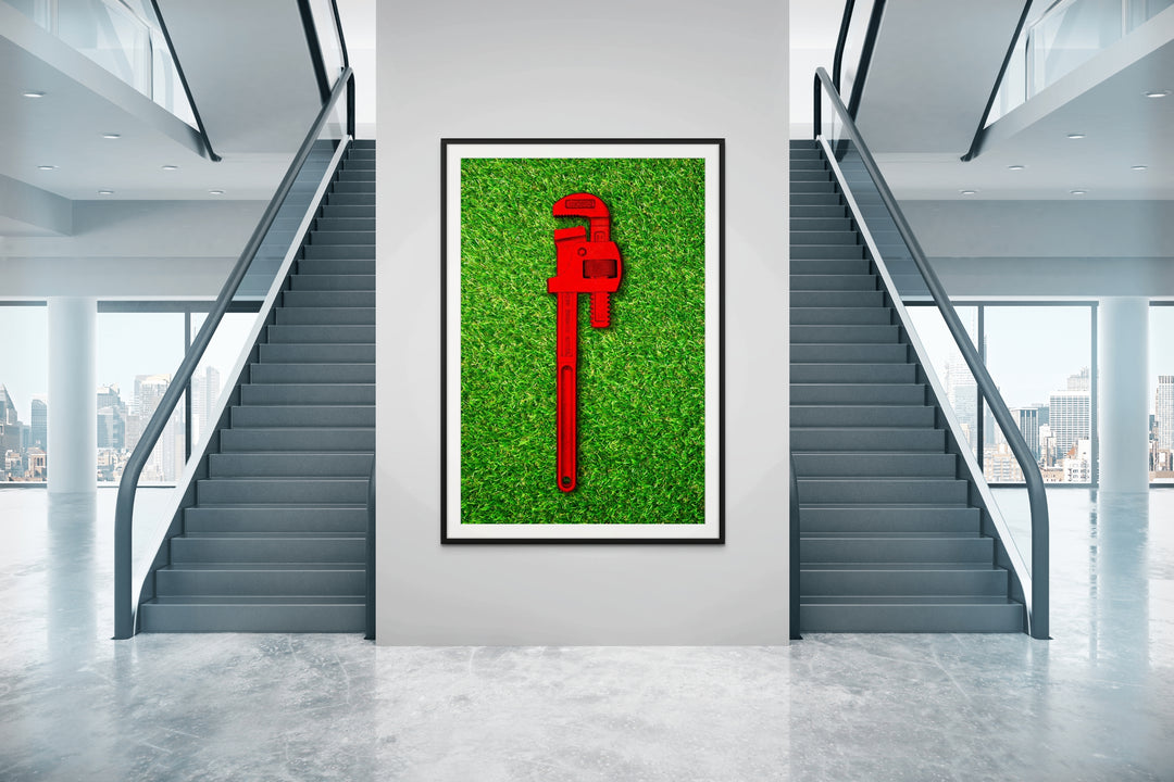 Photograph of a bold red pipe wrench laid flat on vibrant green grass, contrasting industrial form with natural texture.