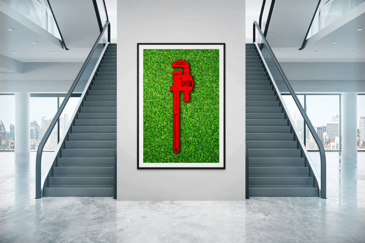 Photograph of a bold red pipe wrench laid flat on vibrant green grass, contrasting industrial form with natural texture.