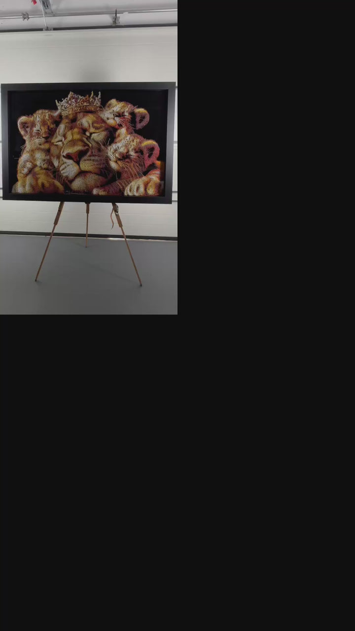 A richly textured injected-scribble artwork depicting a majestic lion wearing a crown, resting peacefully with three lion cubs nestled against him. The composition glows with warm tones of gold, amber, orange and cream, set against a deep black background that enhances the dimensional, thread-like detailing.