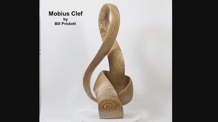 Hand-carved birch plywood sculpture by Bill Prickett combining a treble clef and Möbius strip into a continuous, flowing form, with layered wood grain revealing an infinity loop inspired by music and mathematics.
