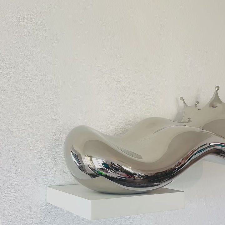 Video - Polished stainless steel sculpture by Yoni Alter capturing the elegant moment of a liquid droplet mid-bounce. The reflective form twists fluidly to the left, with raised crown-like peaks suggesting impact and motion. A sculptural meditation on impermanence and form, grounded by a hidden counterweight for stability.