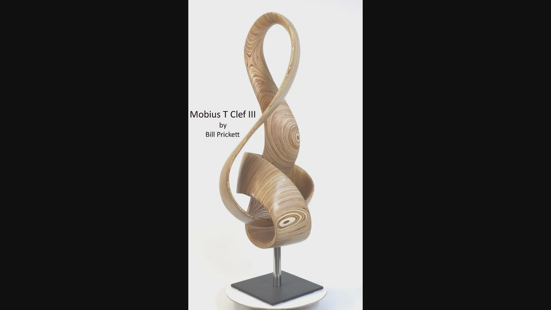 Video of hand-carved birch plywood sculpture by Bill Prickett combining a treble clef and Möbius strip into a continuous, flowing form, with layered wood grain revealing an infinity loop inspired by music and mathematics.