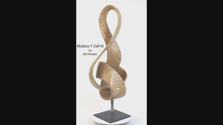 Video of hand-carved birch plywood sculpture by Bill Prickett combining a treble clef and Möbius strip into a continuous, flowing form, with layered wood grain revealing an infinity loop inspired by music and mathematics.