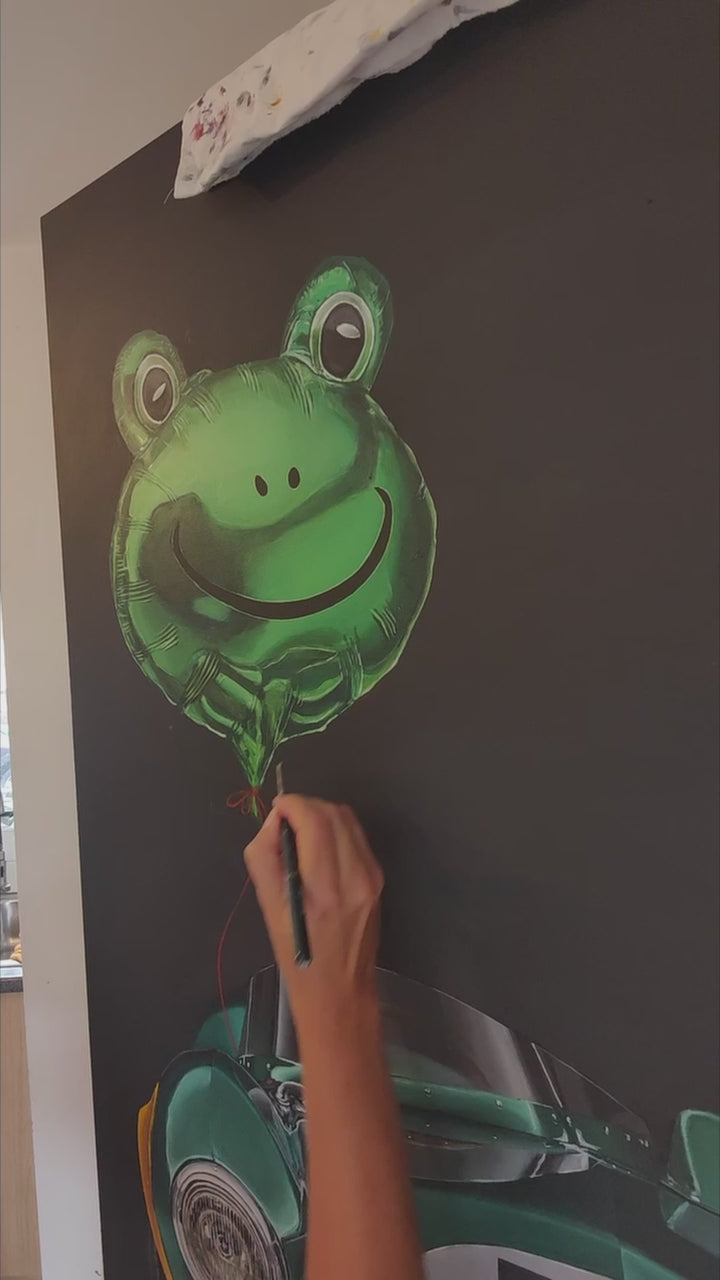 Video of hyper-realistic painting of a classic British racing green Aston Martin DB3S front-on against a deep black background, with a shiny metallic green frog-shaped balloon floating above the car, its red string tied to the vehicle — a playful contrast of automotive heritage and childlike whimsy.