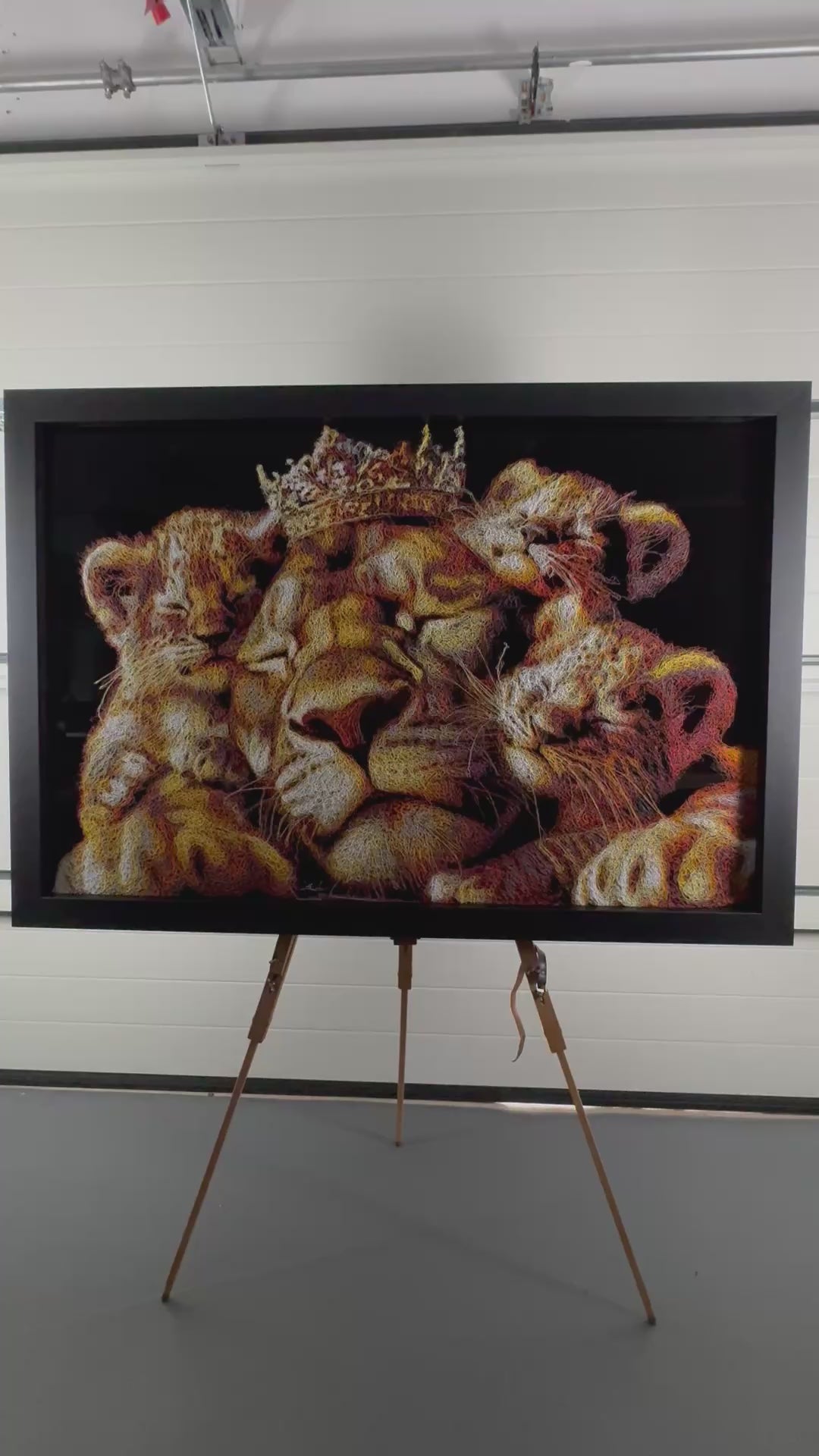 A richly textured injected-scribble artwork depicting a majestic lion wearing a crown, resting peacefully with three lion cubs nestled against him. The composition glows with warm tones of gold, amber, orange and cream, set against a deep black background that enhances the dimensional, thread-like detailing.
