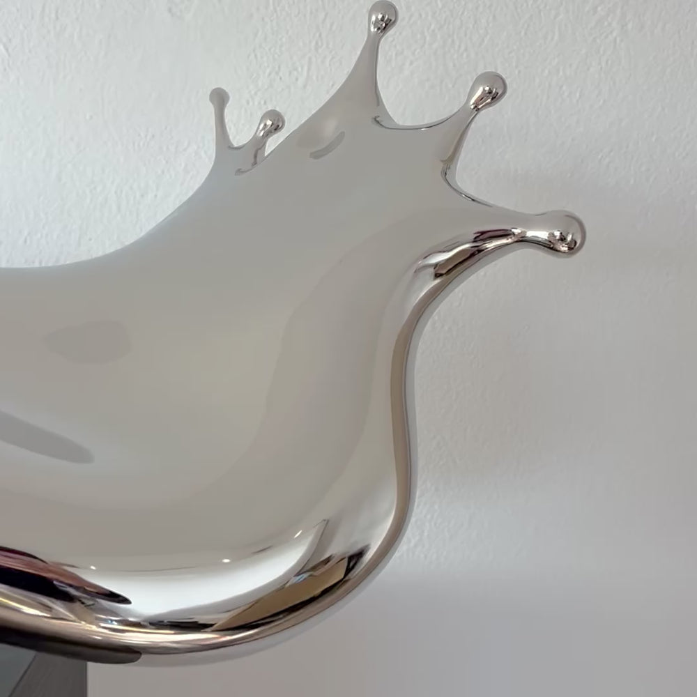 Video - Polished stainless steel sculpture by Yoni Alter capturing the elegant moment of a liquid droplet mid-bounce. The reflective form twists fluidly to the left, with raised crown-like peaks suggesting impact and motion. A sculptural meditation on impermanence and form, grounded by a hidden counterweight for stability.