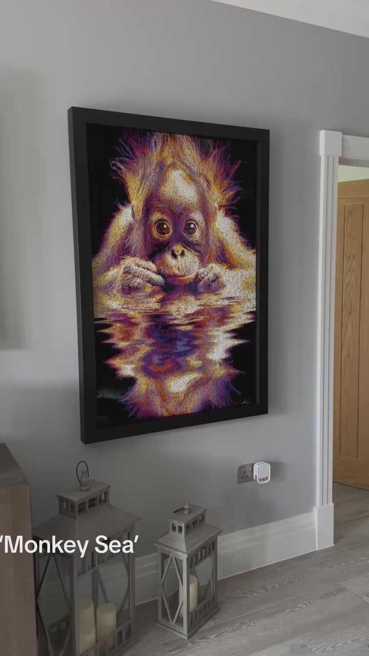 A vibrant textured artwork of a baby orangutan leaning over shimmering water, created with Zalini’s intricate injected-scribble technique, featuring flowing multicoloured lines, bright orange fur, vivid purples and blues, and a mirrored reflection across a glossy black surface.