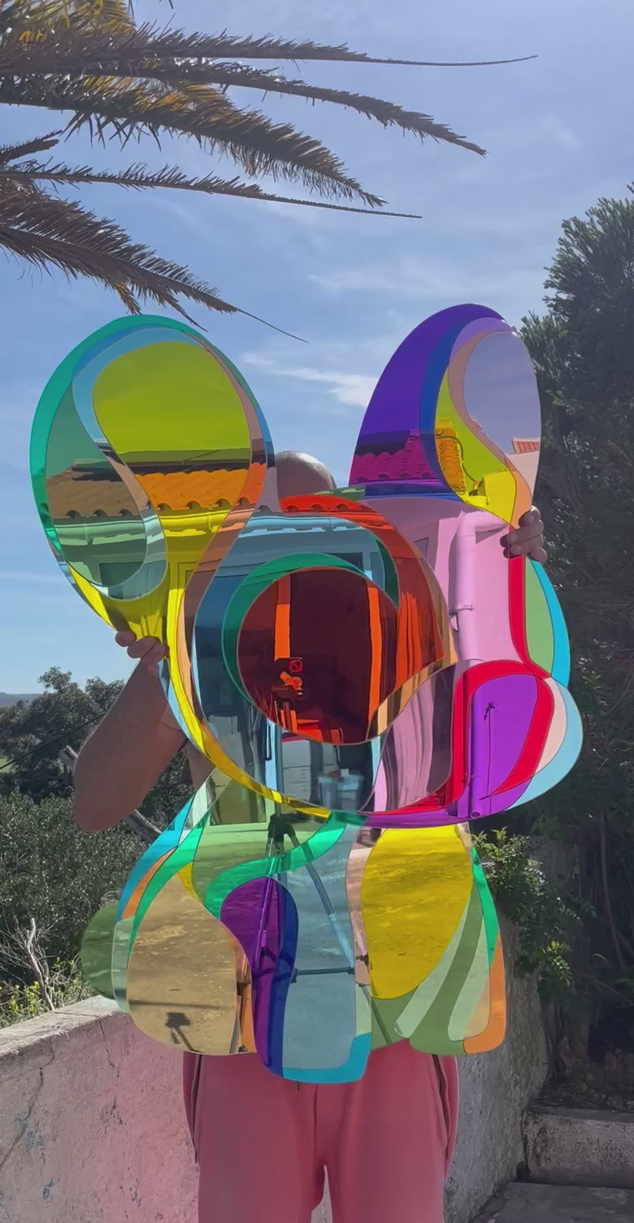 Vibrant, multi-coloured wall sculpture by Yoni Alter in the shape of a stylised French Bulldog, crafted from layered acrylic mirrors with bold, fluid contours and a high-gloss finish. The reflective surfaces create playful distortions of light and environment, merging pop art energy with contemporary design.
