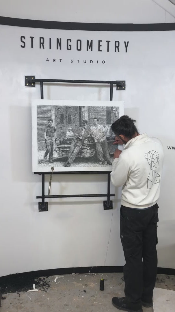 Monochrome nail and string artwork depicting a 1950s street scene with four young men in vintage attire leaning on a classic American car.