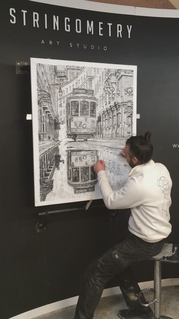 Intricate monochrome nail and string artwork of a Lisbon tram gliding through a historic street, with its reflection perfectly mirrored in a wet cobbled road.