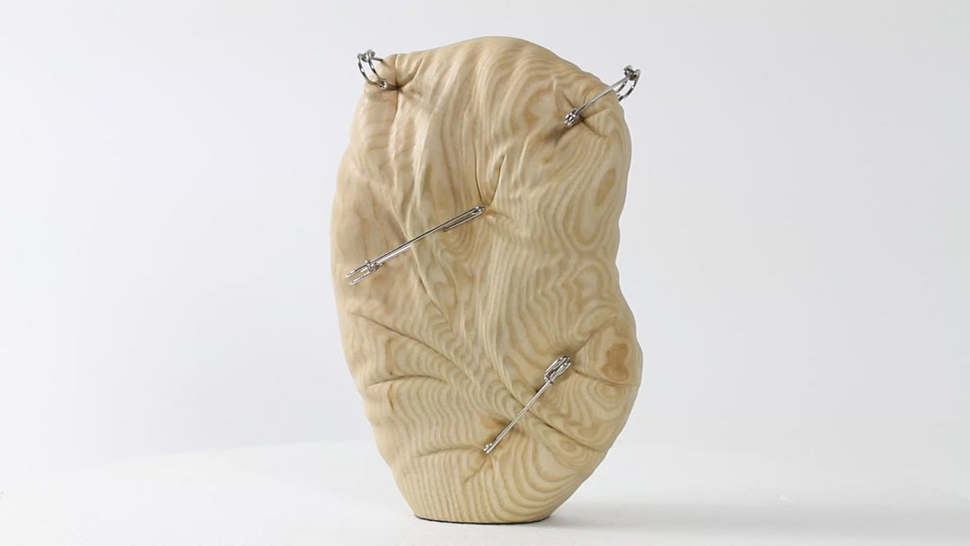 Hand-carved abstract wood sculpture in ash by Bill Prickett, featuring softly contoured organic form pierced with steel pins, creating a visual tension between solid wood and restrained compression.