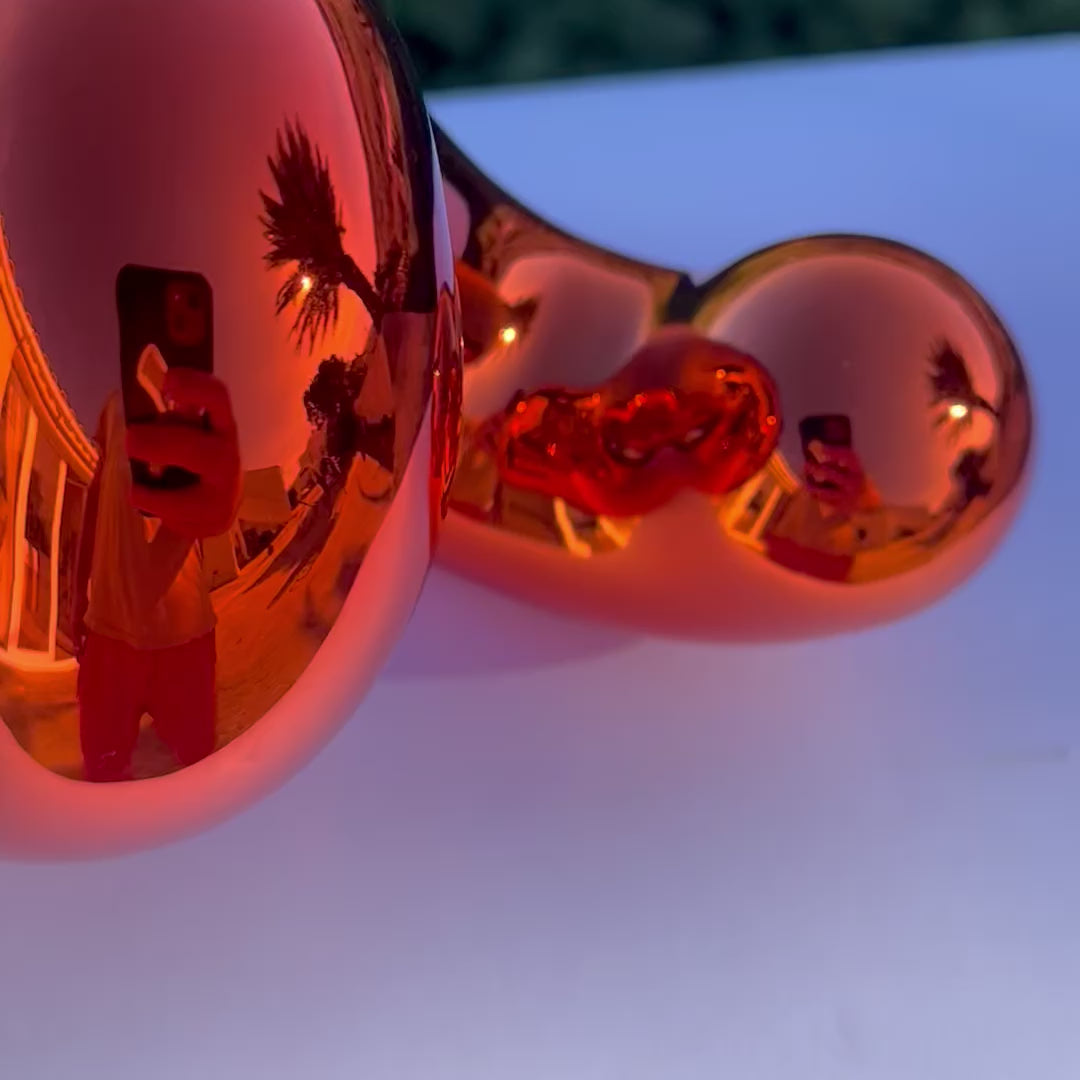 Freestanding sculptural artwork spelling ‘LOVE’ in a flowing, cursive form, finished in high-gloss orange-tinted stainless steel.
