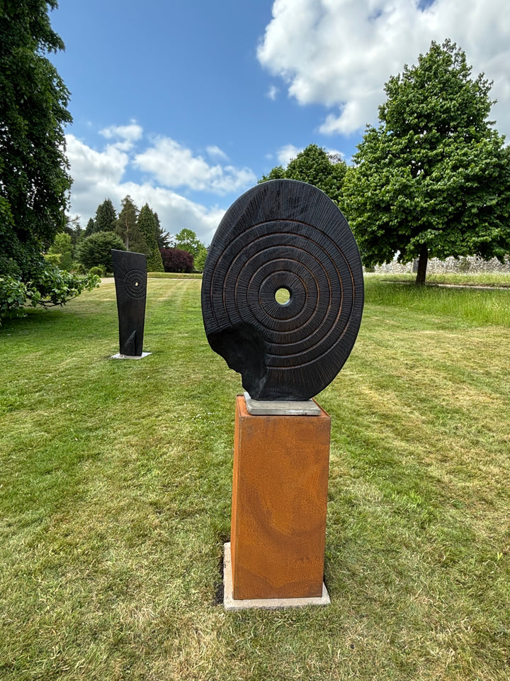 Charred oak sculpture by Glen Farrelly titled Ritual, carved with concentric cup and ring markings around a central void. Blackened Yakisugi surface contrasts with golden highlights, evoking ancient standing stones and ritual energy.
