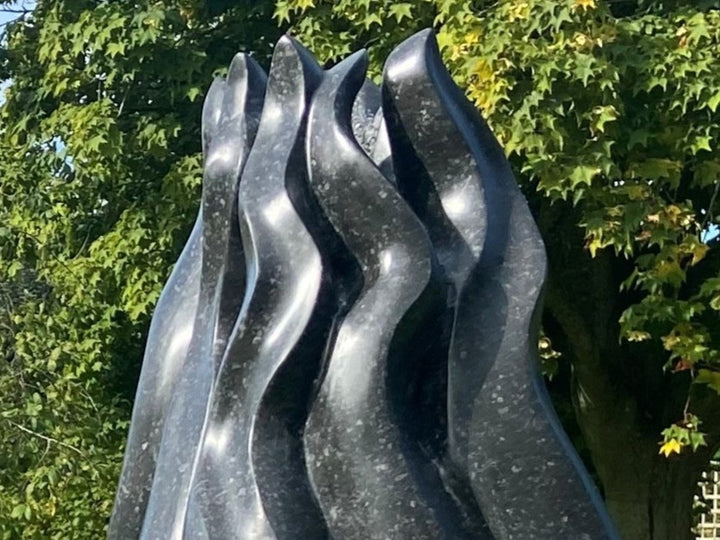 Tentacle by Brendan Cullen, a hand-carved Kilkenny fossilised limestone sculpture with smooth, flame-like tendrils rising upward from a rounded base, transitioning from pale speckled grey to deep polished black, suggestive of organic growth or movement frozen in stone.