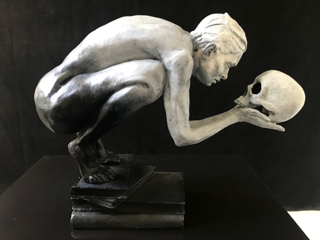 Teresa Wells’ The Prophecy (2024), limited edition bronze sculpture depicting a crouched, nude figure balanced atop stacked books, holding a human skull in both hands and gazing intently into its hollow eyes. Finished in a pale grey patina with darker shading to emphasise musculature and contours, the piece evokes themes of mortality, knowledge, and forewarning. At 30cm × 25cm × 49cm and 23.4kg, it combines fine anatomical detail, symbolic elements, and a contemporary reinterpretation of classical imagery.